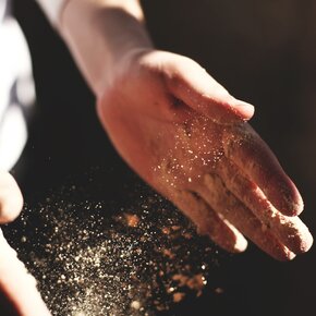 Eine Hand streut Saatgut auf die Erde